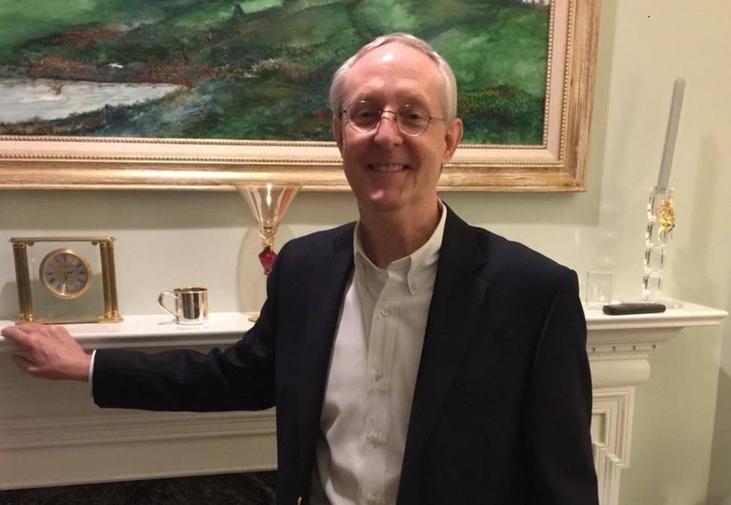 GCU Alumnus Dr Willam Mayfield standing in front of his fireplace