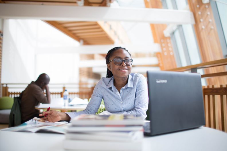 Student with books studying and laptop at Glasgow Caledonian University