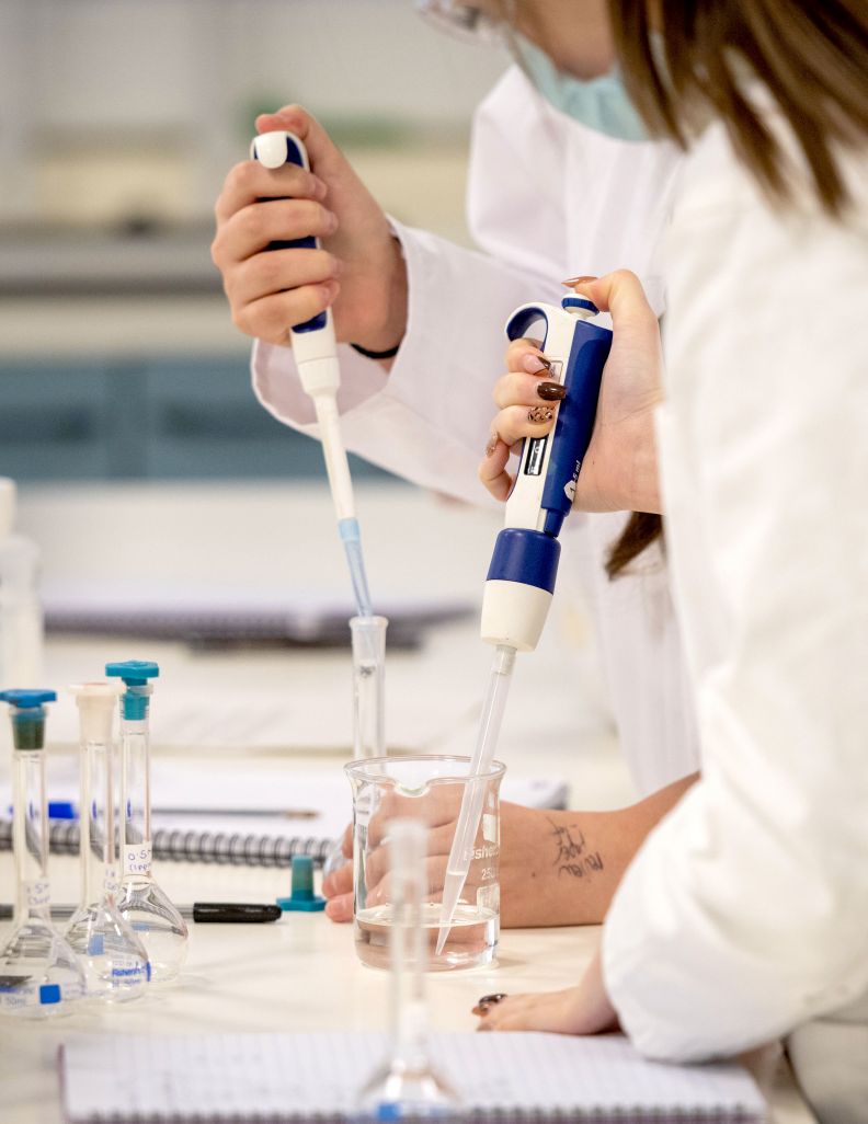 A close up of two students' hands squeezing pipettes into a test tube and beaker of liquid.