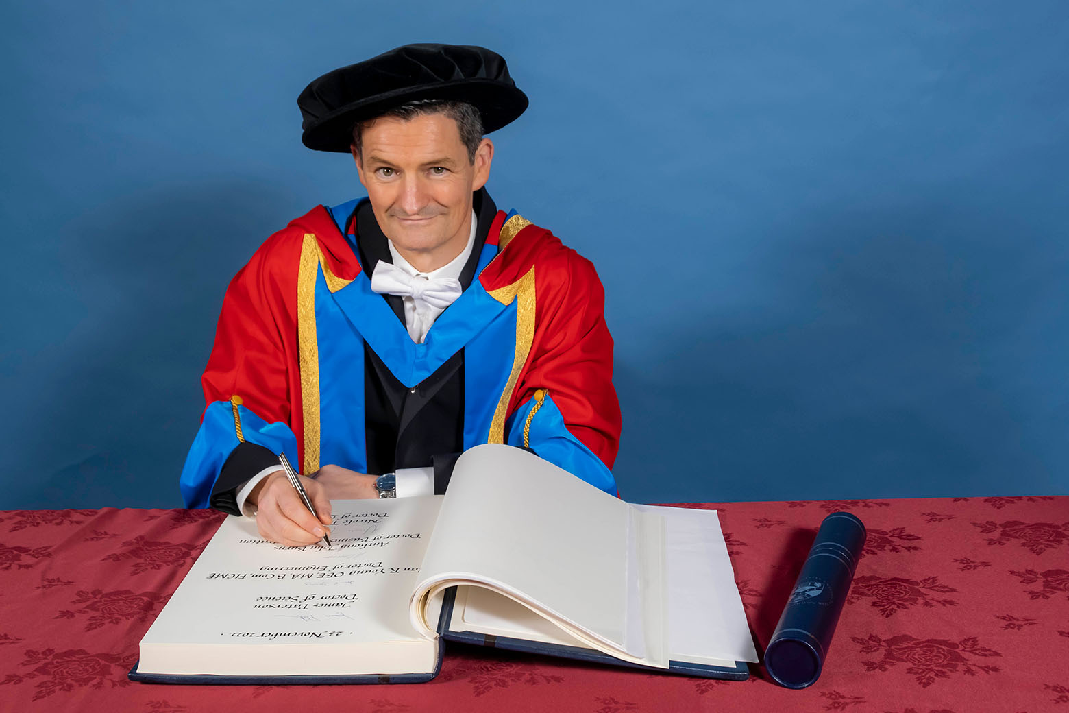 GCU Honorary Graduate Dr Anthony Burns signing a book in graduation hood and hat