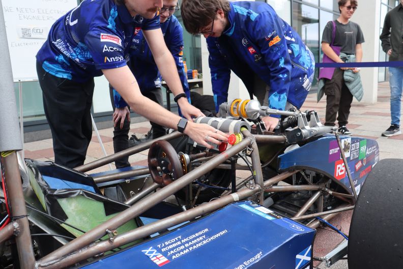 Close up of three pairs of hands working on a blue racecar.