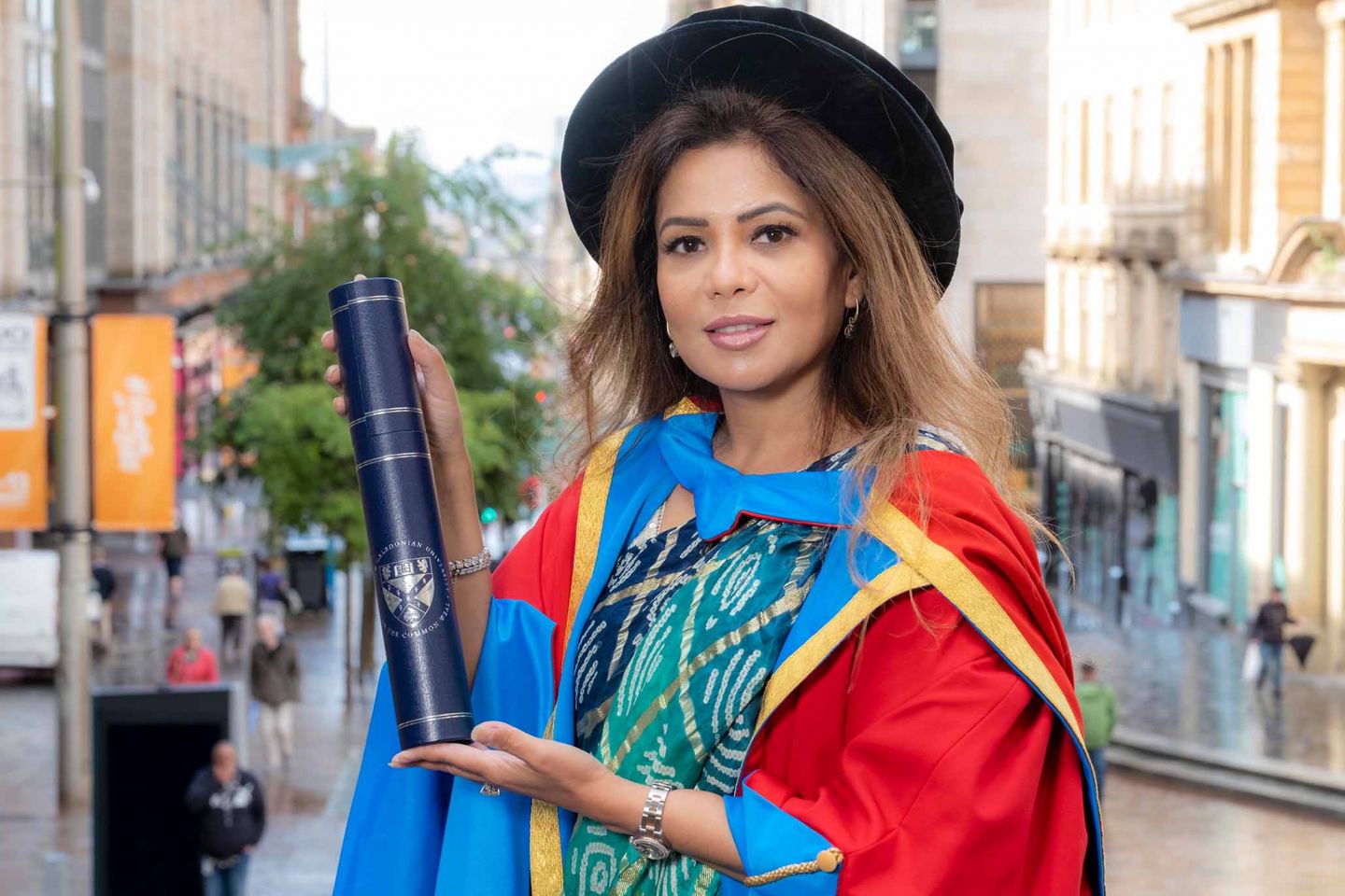 GCU Honorary Graduate Dr Poonam Guptai n graduation gown and hat, holding a degree parchment container