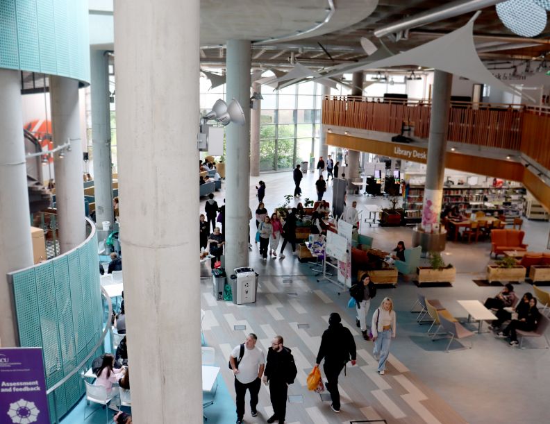 A view from the second floor down to the Sir Alex Ferguson library where a crowd of people are milling about.