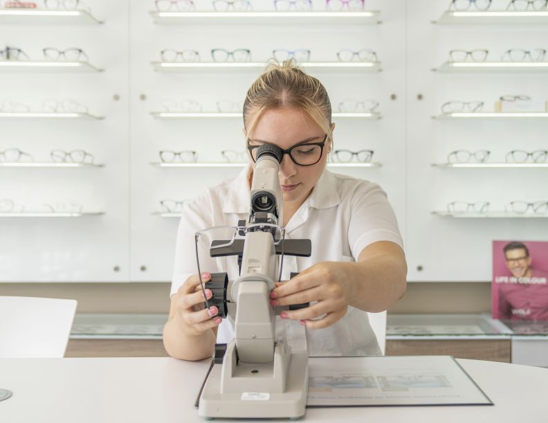 A young female student inspects a pair of glasses lenses in a lensmeter.