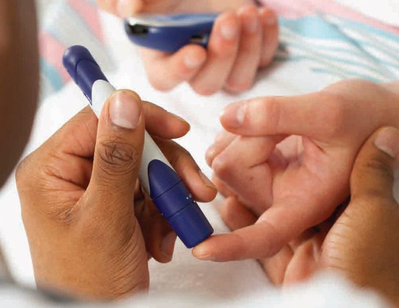 A pair of hands uses a blood glucose level monitor on another pair of hands.