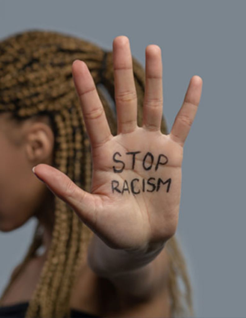 Person standing with head down and the words STOP RACISM written on their hands